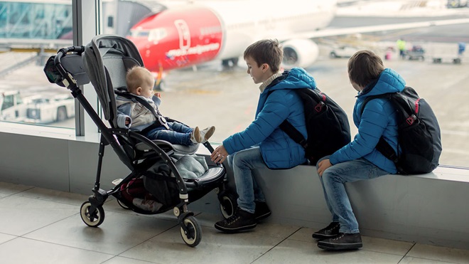 two children and baby in a travel stroller waiting at airport